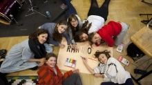 zdjęcie dziewczynek uczestniczących w warsztatach z tutorką Olą Rzepką. Wspólnie tworzą plakat zespołu. Śmieją się. Widać fragment napisu Rainbo... na plakacie