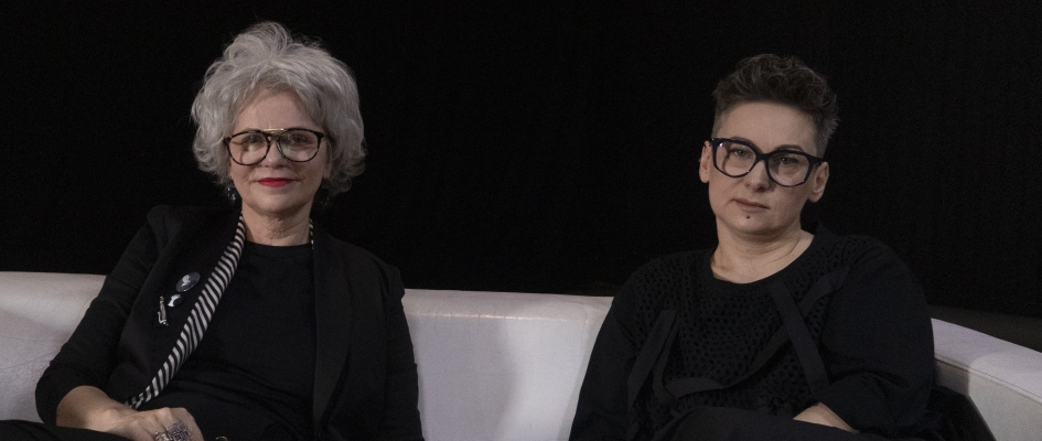 Małgorzata Wandasiewicz i Sylwia Jaworska (obydwie ubrane na czarno) siedzą na białej, skórzanej kanapie
