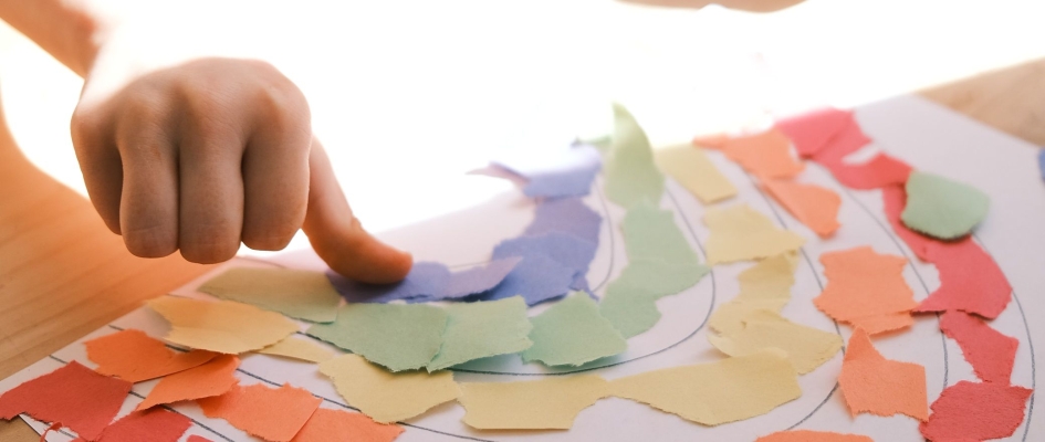 fragment zdjęcia, widać dziecięcą dłoń, która tworzy kolaż-tęczę na papierze. Photo by Taylor Heery on Unsplash
