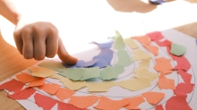 fragment zdjęcia, dziecięca dłoń tworzy kolaż - tęczę na papierze