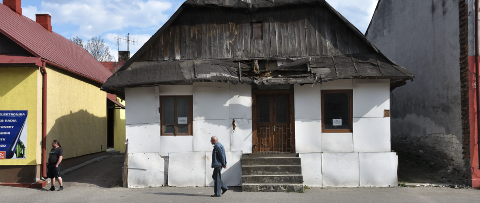 Szczebrzeszyn, stara waląca się niezamieszkana chałupa w środku miasta. Bielone ściany, walący się dach, przechodnie.