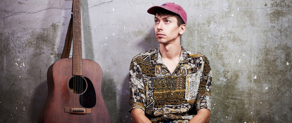 Michał wpatrzony w dal, obok gitara na tle ściany